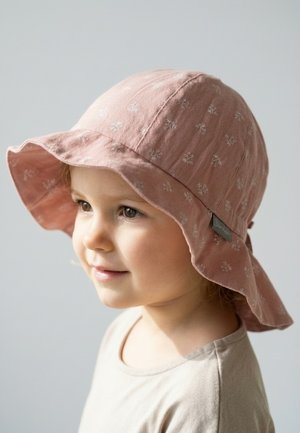 Bambino piccolo che indossa un cappello a tesa larga rosa chiaro con piccoli motivi floreali bianchi, sorridente e che guarda leggermente verso sinistra.