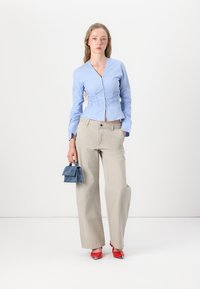 Light blue fitted blouse with gathered sides, beige wide-leg pants, red pointed-toe heels, and a small blue suede handbag.