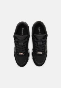 Czarne sneakersy z mieszanką matowych i teksturowanych materiałów. Cechy to sznurowane zapięcie, akcenty logo oraz biała podeszwa. Wyraźne elementy designu to gładkie wykończenie i subtelne oznakowanie.