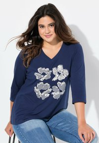 Marinblå V-halsad tröja med trekvartslånga ärmar, prydd med ett strukturerat blommönster i vitt och randiga detaljer.