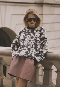 Gezellige, gebloemde trui in marineblauw en crèmekleur, gecombineerd met een gestructureerde, geplooide roze rok. Zonnebril maakt de outfit compleet.