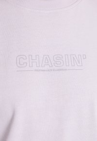 Šviesiai rožinė džemperis su apvalia iškirpte, pagamintas iš minkštos medžiagos, su iškeltu tekstu "CHASIN' PERFORMANCE JEANSWEAR."