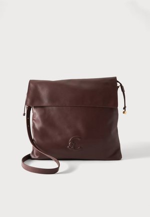 Sac à bandoulière en cuir marron foncé avec rabat, sangle réglable et logo embossé sur le devant sur un fond clair uni.