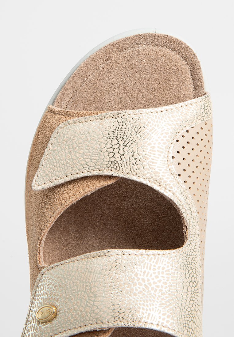Sandalo marrone con accenti metallici dorati, caratterizzato da due cinturini regolabili, morbida texture in suede e dettagli perforati. Design minimalista.