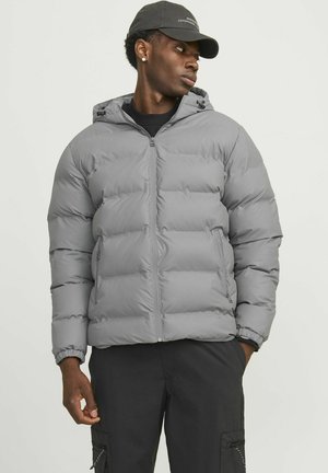 Gray puffer jacket featuring a zip front, quilted design, and hood, with elastic cuffs and side pockets, worn over a black top.