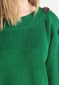 Maglione verde lavorato a maglia con una trama a coste, scollatura ampia e bottoni decorativi sulla spalla. Presenta una vestibilità rilassata.