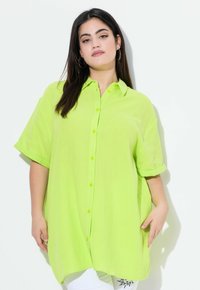 Camicia button-up oversized verde lime con maniche corte e tessuto testurizzato. Presenta un colletto e un orlo dritto con fessure laterali.