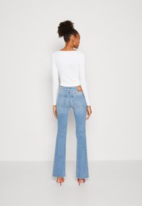 Vit långärmad topp i kombination med ljusblå utsvängda jeans, med en bakfickdetalj och färgglada högklackade skor.