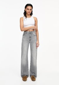 Jeans grii cu picioare largi și talie înaltă, având un design clasic cu cinci buzunare și o ușoară decolorare. Asortați cu un top alb, ajustat.