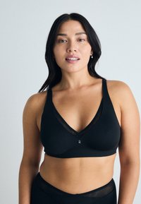 Soutien-gorge noir avec un design en V, mettant en avant un tissu doux, des accents en maille transparente et un petit détail décoratif central. Texture lisse dans l'ensemble.