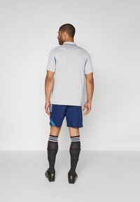 Lysegrå polo skjorte med korte ærmer, parret med mørkeblå shorts. Sorte knæstrømper med hvide striber og sorte fodboldstøvler.