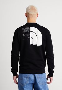 Felpa nera con maniche lunghe e polsini a coste. Presenta un grande logo bianco sul retro e testo in un carattere moderno.