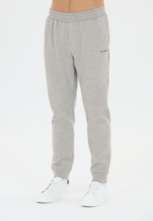 Mand iført lysegrå joggingbukser med elastisk talje og manchetter, kombineret med hvide sneakers på hvid baggrund.