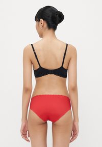 Black lace-trimmed bra with adjustable straps, paired with red scalloped-edge panties, showcasing smooth fabric and contrasting colors.