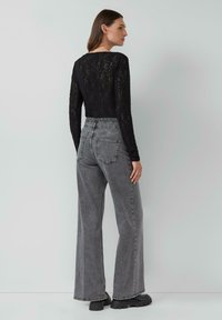 Schwarzes Spitzenoberteil mit langen Ärmeln, kombiniert mit grauen, hoch-taillierten, weiten Jeans. Strukturierter Stoff und lässiges Design mit auffälligen Gesäßtaschen.