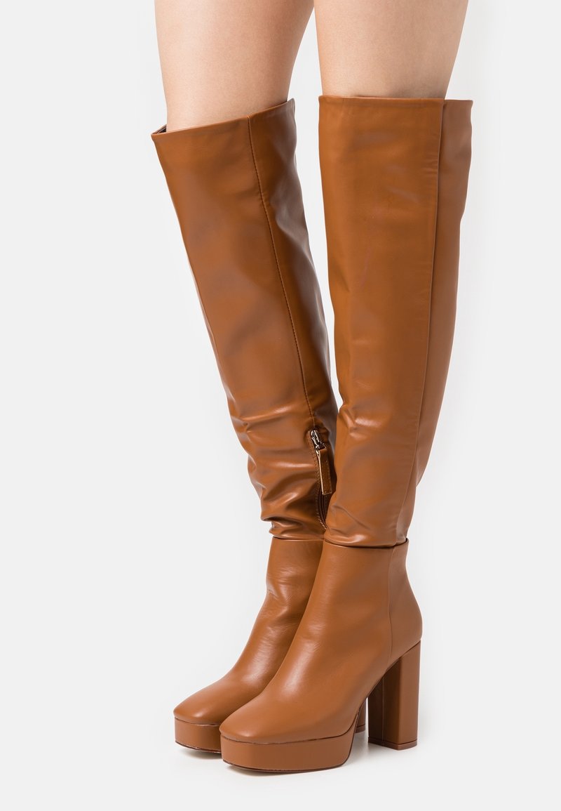 Bottes montantes en cuir synthétique marron lisse, avec un talon bloc, une semelle plateforme et une fermeture éclair sur le côté pour un enfilage facile.