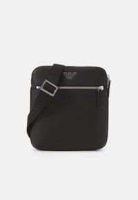 Borsa crossbody nera con tracolla regolabile, tasca con zip frontale e emblema logo argento al centro in alto.