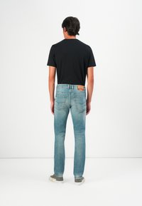 Vaqueros de denim azul claro con corte ajustado, que presentan un parche de cuero en la cinturilla trasera, combinados con una camiseta negra de manga corta.