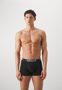 Schwarze Baumwoll-Boxershorts mit einem elastischen Bund, der ein weißes Adidas-Logo und ein Design mit drei Streifen aufweist. Glattes Material, körperbetonter Schnitt.