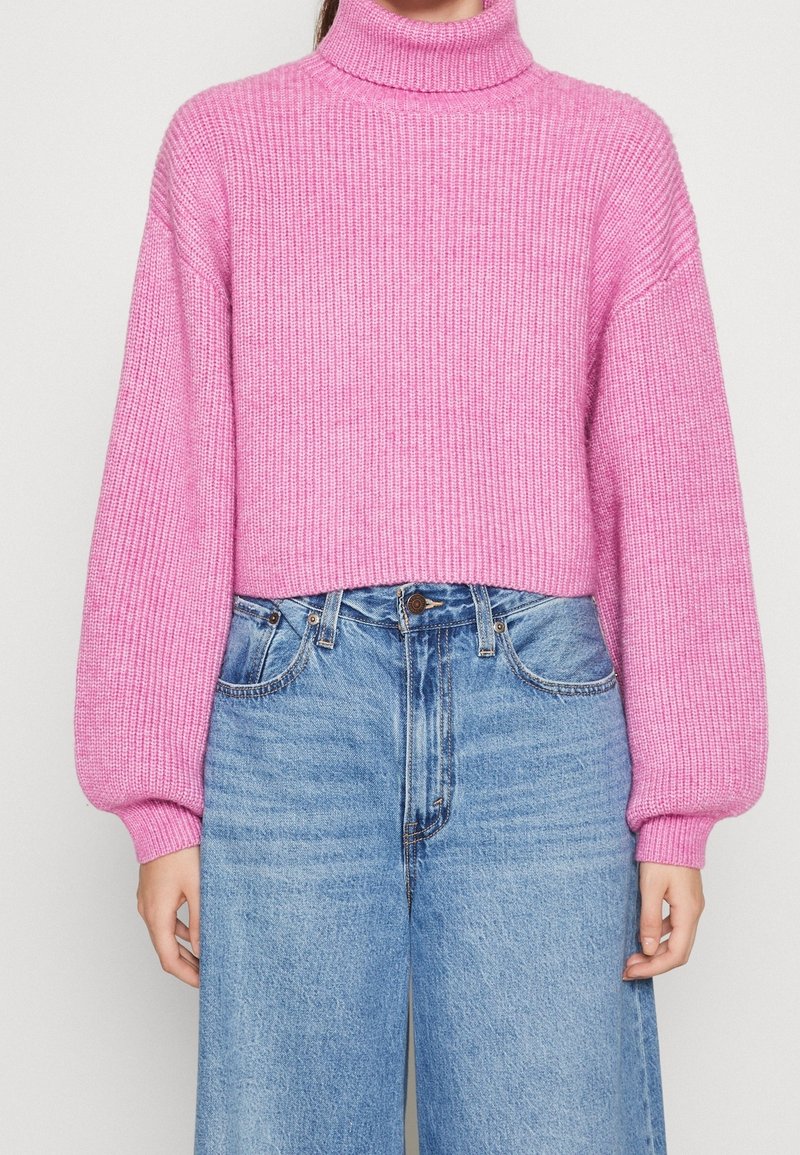 Pull à col roulé côtelé rose avec manches ballon, coupe courte, associé à un jean droit taille haute bleu clair.