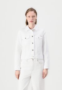Hvit denimjakke med krage, lange ermer, brystlommer og sølvknapper; kombinert med matchende hvite bukser. Jevn tekstur.