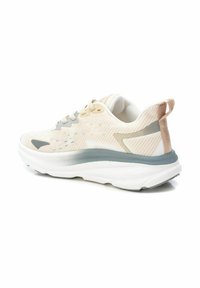 Zapatilla con una parte superior texturizada de beige claro, acentos grises, suela blanca acolchada y una pestaña en el talón para facilitar su uso.