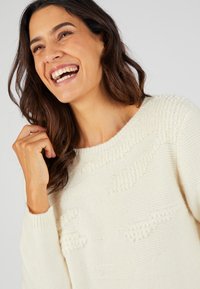 Pull en maille crème clair avec des motifs texturés, col rond et manches longues, mettant en valeur un matériau doux et confortable.