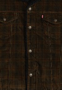 Brown corduroy jacket with a textured surface, featuring metal snap buttons, two chest pockets, and a black inner lining.