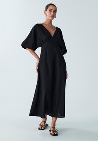 Black maxi dress with a deep V-neck, puff sleeves, and a fitted bodice. Made of lightweight fabric, featuring a smooth texture.