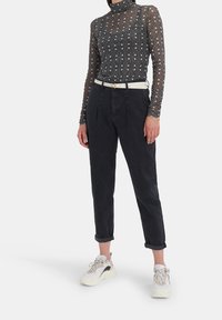 Musta kuvioitu pitkähihaisen paita, jossa on korkea kaulus, yhdistetty korkeavyötäröisiin tummiin housuihin ja valkoisiin lenkkarit harmailla yksityiskohdilla ja nauhoilla.