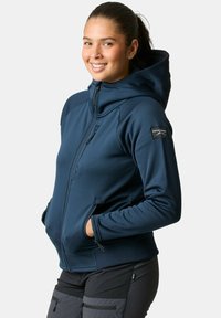 Marineblauwe fleece hoodie met een rits aan de voorkant, een getailleerd ontwerp en een grote capuchon. Voorzien van zijzakken en een merkpatch op de mouw.