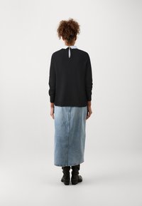 Suéter negro de manga larga con un detalle de ojal en la parte posterior, combinado con una falda de mezclilla azul clara. Botines negros completan el conjunto.