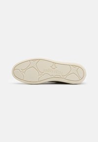 Suela de zapato con un agarre de goma texturizado color crema que presenta una banda de rodadura con patrón y la marca "PETER KAISE" en relieve en la superficie.