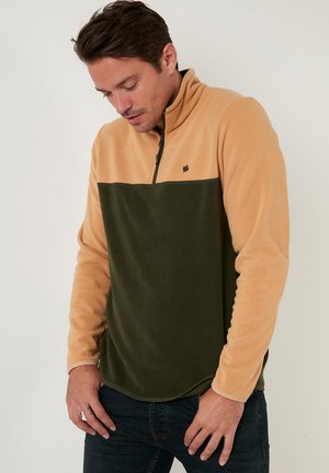 Fleece-pullover med en tan øverste halvdel og grøn nederste halvdel, med lynlåskrave og diskret logo detaljer på brystet. Blød tekstur og buet kant.