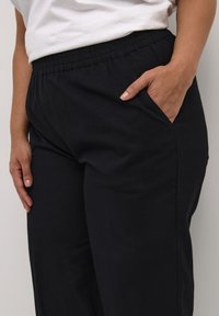 Pantaloni neri con elastico in vita e tasche laterali. Tessuto morbido, vestibilità comoda e design a gamba dritta. Aspetto semplice e versatile.