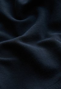 Marineblauer Stoff mit einem strukturierten Rippenmuster, der weiche, wellenförmige Falten und einen subtilen Glanz zeigt. Die glatte Textur betont Tiefe und Bewegung.