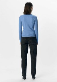 Ljusblå ribbad tröja med en figurnära silhuett, ihop med svarta denimjeans. Outfiten har en klassisk rund halsringning och långa ärmar.