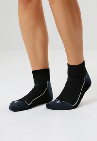 Svarta ankelsockor med ribbat manschett, grå accenter och ljusa sömnadsdetaljer. Tillverkade av ett flexibelt, andningsbart material.