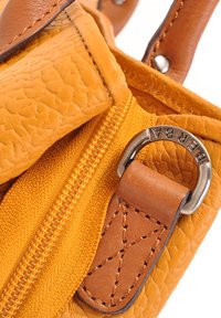 Detail van een gele leren tas met een gestructureerd oppervlak, bruine accenten op de banden en een metalen ring met het merk "BERBA." Zichtbare ritsaccenten.
