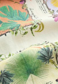 Tissu avec des imprimés botaniques colorés, comprenant de grandes feuilles vertes, des vignes et du texte sur un fond crème clair.
