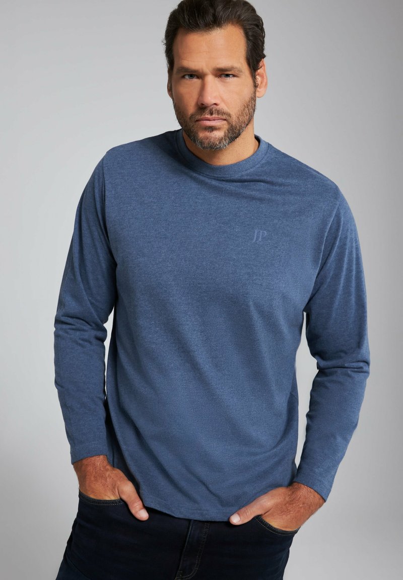 Dlouhý rukáv modré tričko vyrobené z měkké tkaniny, s kulatým výstřihem a jemným logem na prsou. Texturovaný povrch.