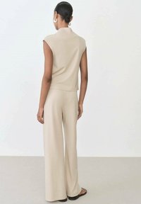 Beige sleeveless top with a rounded collar paired with matching wide-leg pants. Smooth fabric texture; minimalistic design with no patterns.
