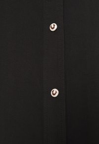 Camisa negra con una botonera en el frente con botones blancos en contraste, tejido texturizado y sutiles detalles de costura a lo largo de las costuras.