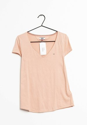Beige Tommy Jeans T-shirt met korte mouwen en V-hals, hangend aan een zwarte hanger met prijskaartje tegen een witte achtergrond.