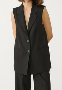 Schwarzer ärmelloser Blazer mit taillierter Passform, ausgestattet mit einem Reverskragen, zwei Fronttaschen und zwei Knöpfen. Glatte Textur mit matter Oberfläche.