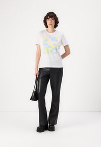 White cotton t-shirt featuring a pastel geometric print. Paired with black faux leather wide-leg pants and black platform shoes.