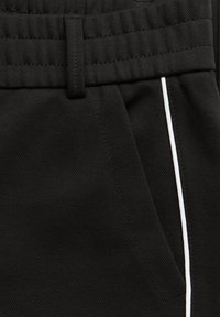 Černé sportovní šortky s texturovanou látkou, elastickým pasem a bílým proužkem na straně u kapsy.