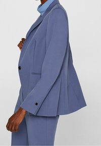 Ljusblå skräddarsydd kavaj med enstaka knäppning, spetsiga slag och strukturerad passform. Har en framficka och ärmsnappar.