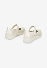 Zapatos Mary Jane de color beige claro con parte superior de punto texturizado, acentos metálicos y correa de Velcro; cuentan con una suela acolchada para mayor comodidad.