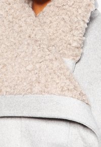 Cappotto di lana grigio con un ampio colletto di pile beige testurizzato. Il colletto ha un aspetto soffice e morbido, migliorando il design complessivo del capo.